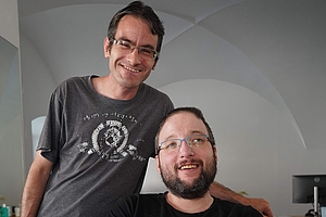 Helmut Wieser steht hinter dem sitzenden Marcel Schäfer und hat seinen Arm um dessen Schulter gelegt.